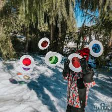 Image of a snow covered ground and paperplates with colored paper in the center hanging from a tree.