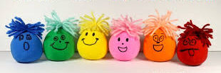 An image of multi colored balloons that fit in a hand with silly faces drawn on them and yarn on the top for hair.