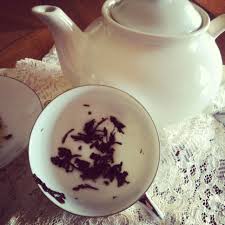 Image of a white tea pot and white tea cup with tea leaves at the bottom.