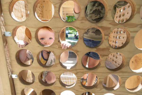 A small child is seen throw holes in an interactive panel on the playscape.