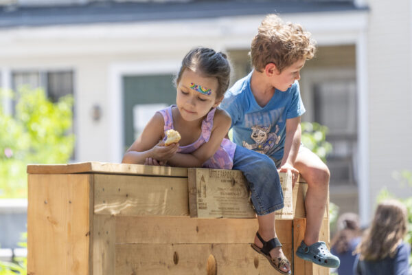 Two kids sit atop a climbing wall on playcape
